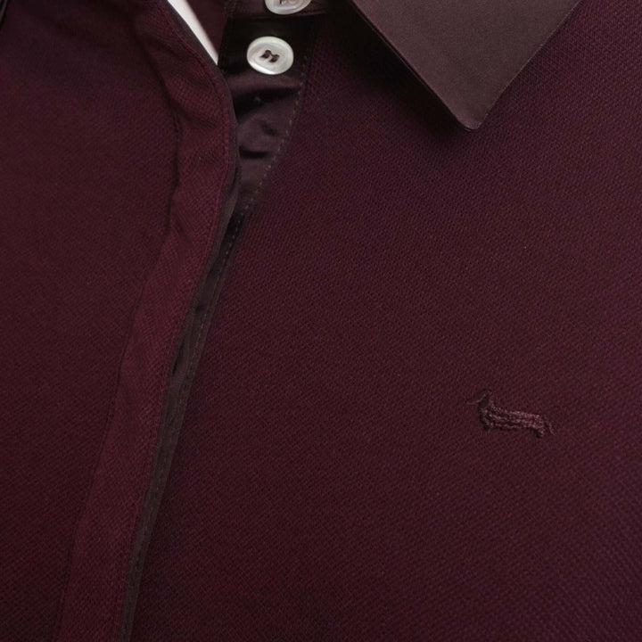 Close-up of a burgundy polo shirt with a brand logo on a dark background