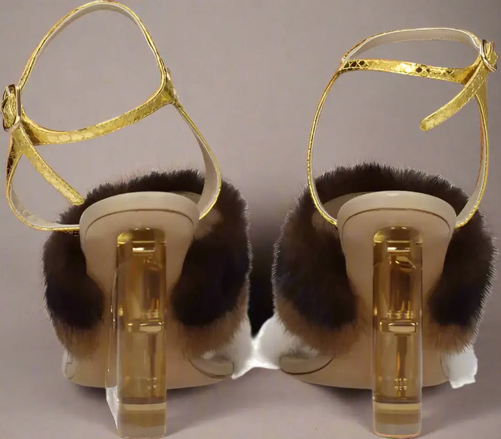 Pair of high-heeled shoes with gold straps and fur accents on a white background