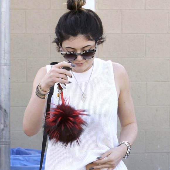 Woman holding a phone with a fluffy red and black accessory, wearing a white sleeveless top.