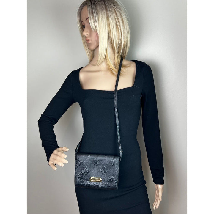 Mannequin wearing a black outfit with a blue textured handbag on a plain background