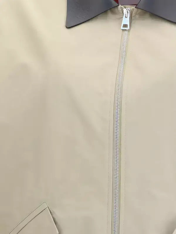 Close-up of a beige jacket with a silver zipper on a light gray background