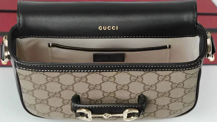 Gucci handbag with monogram pattern and black leather top, on a white background