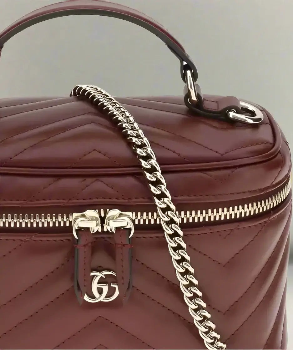 Maroon handbag with gold chain and logo on a white background