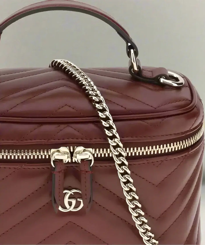Maroon handbag with gold chain and logo on a white background