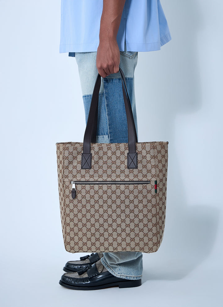 Person holding a patterned tote bag with a visible brand logo on a light gray background
