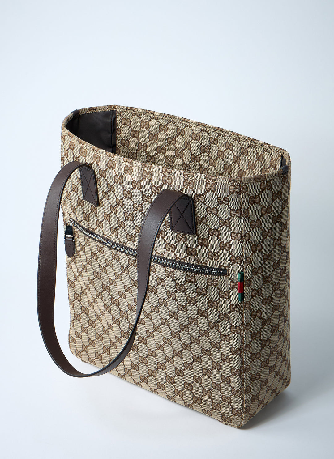 Beige patterned tote bag with brown leather handle on a light gray background