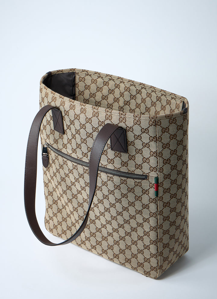 Beige patterned tote bag with brown leather handle on a light gray background