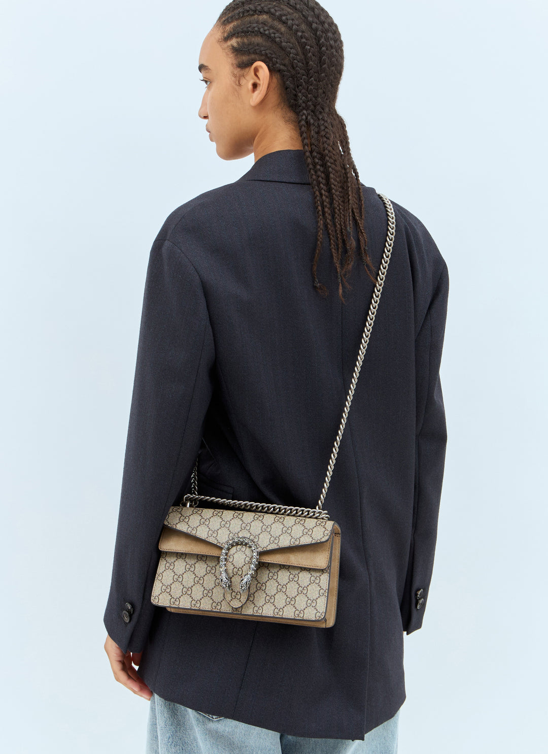 Person wearing a black jacket with a Gucci handbag on a light blue background