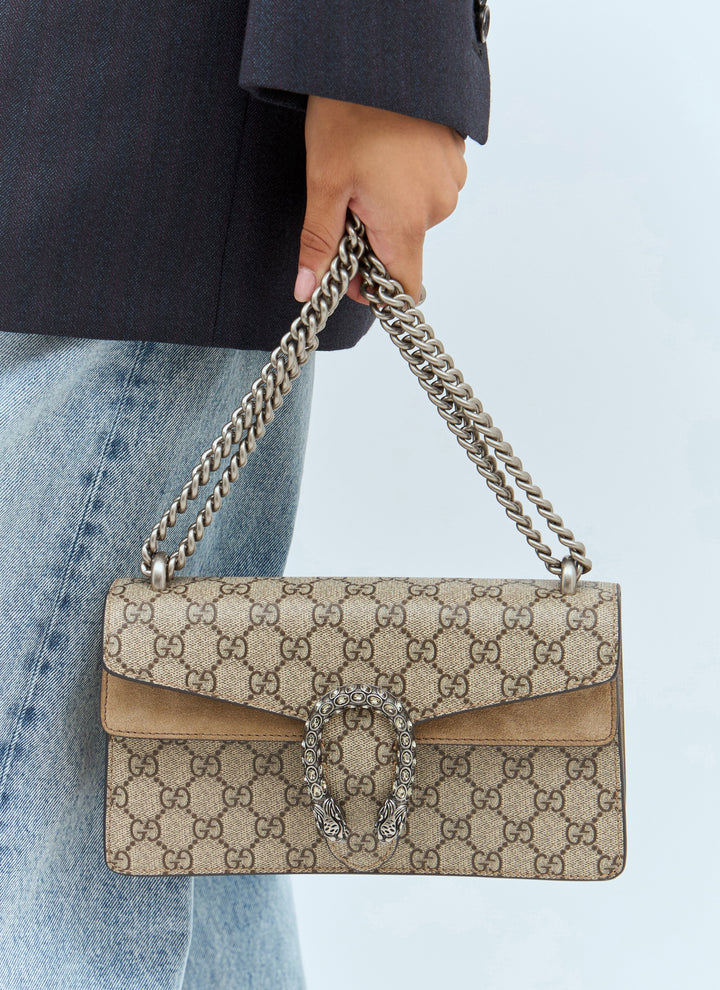 Beige Gucci handbag with chain strap held by a person wearing a dark coat and light blue jeans.