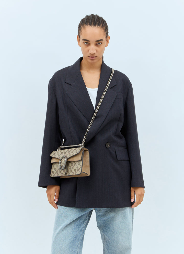 Person wearing a black blazer and light blue jeans, holding a patterned handbag against a light blue background