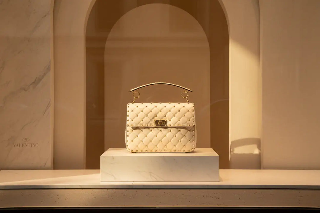 Beige handbag with gold studs and a gold clasp on a black background