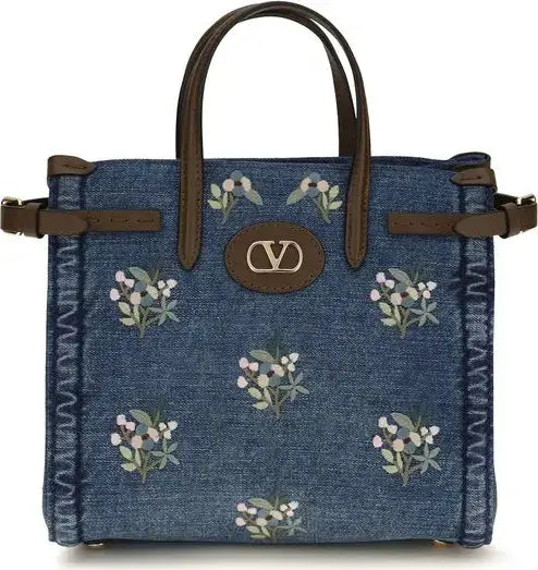 Blue denim handbag with floral patterns and brown straps on a white background
