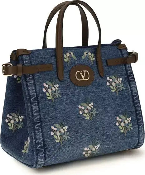 Blue denim handbag with floral patterns and brown leather accents on a white background