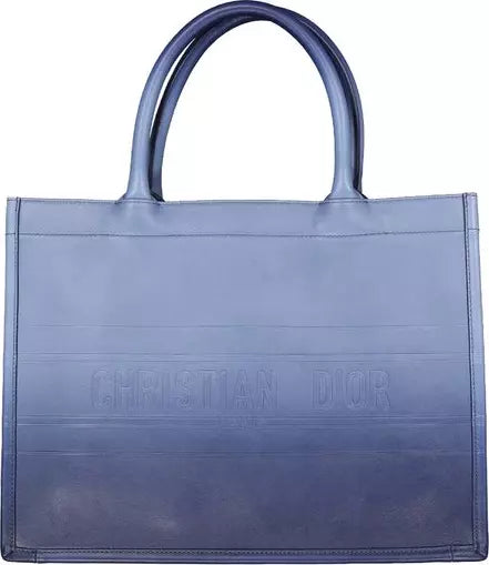 A blue Christian Dior tote bag with embossed branding on the front, featuring dual top handles and a structured rectangular shape, shown against a plain white background.