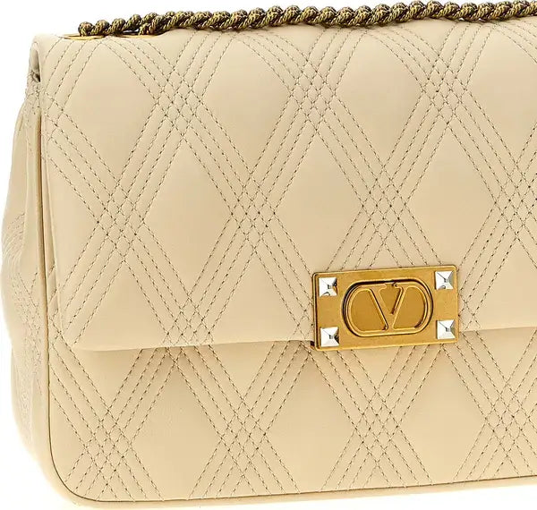 Beige quilted handbag with a gold logo plaque on a white background