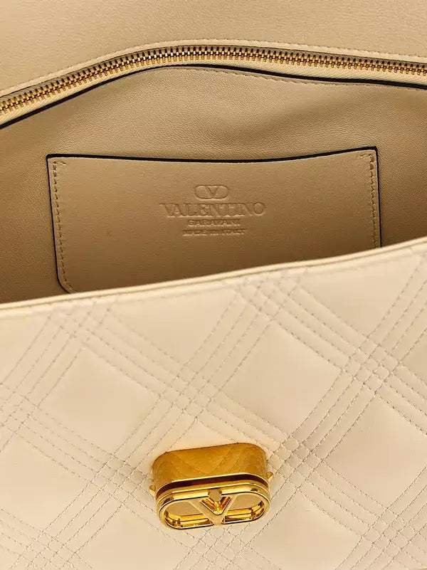 Close-up of a beige handbag with gold zipper and logo, featuring the brand 'Valentino'.