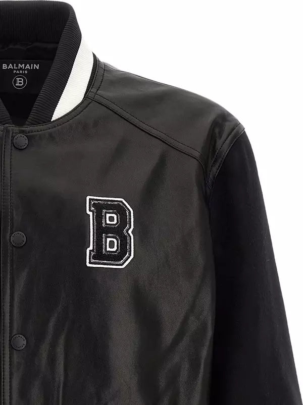 Close-up of a Balmain varsity-style jacket in black with a white striped ribbed collar and a large embroidered white and black letter B on the chest.