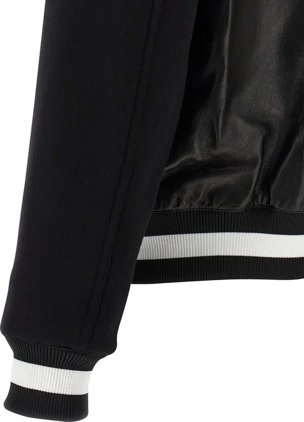 Close-up of a black jacket sleeve and body showing ribbed cuffs with white stripes and a matching white stripe detail near the hem.