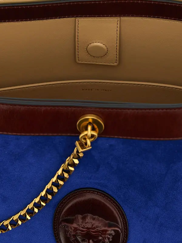 Close-up of a blue handbag with gold chain and brown leather accents.
