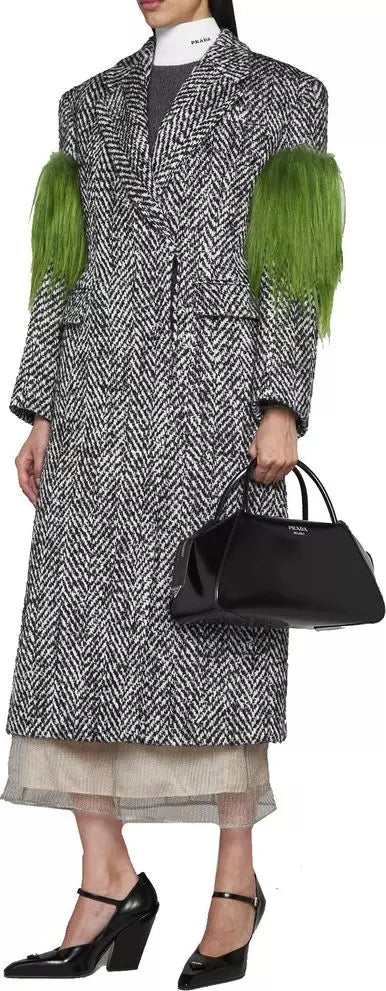 Person wearing a patterned coat with green sleeves and holding a black handbag.
