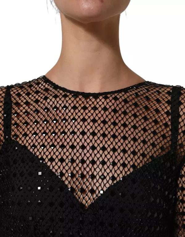 Close-up of a model wearing a black fishnet mesh top with a V-neckline and sequined details, set against a plain white background.