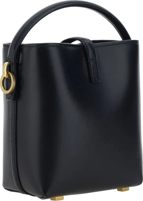 A black leather bucket handbag with a top handle, featuring a distinctive gold-tone interlocking G shape ring on the side and small gold-tone feet at the base, shown against a plain white background.