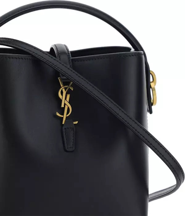Close-up of a black leather handbag with a gold-tone YSL monogram charm and matching gold hardware, shown against a white background.