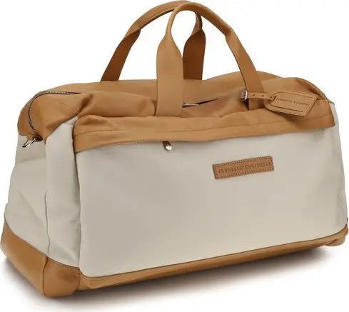 A duffel bag with a cream-colored body and tan leather-like handles, trim, and base. A small rectangular brand patch on the front reads &