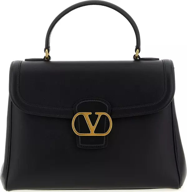 A black leather top-handle handbag with a large gold-tone interlocking V logo clasp on the front, photographed against a plain white background.