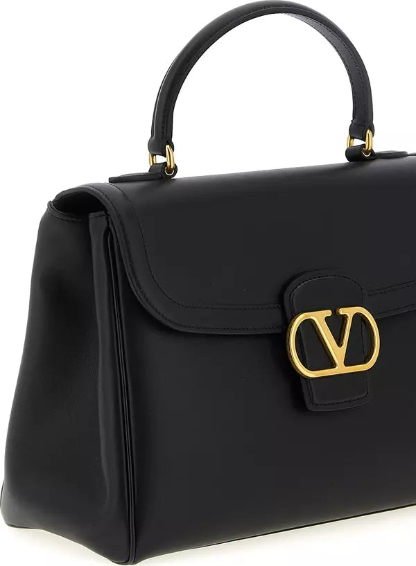 A black leather top-handle handbag with a large gold-tone interlocking V logo clasp on the front, photographed on a clean white background.