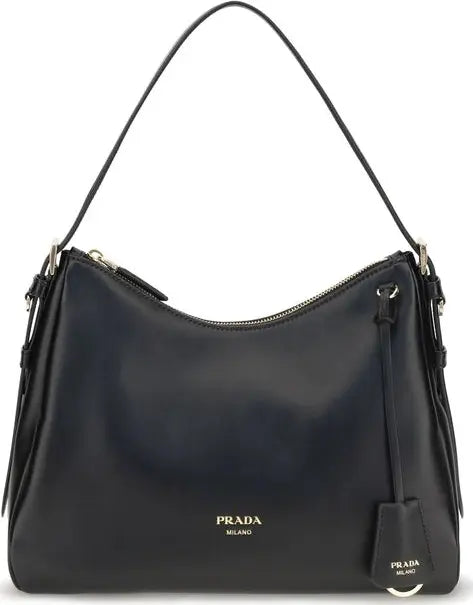 A black leather Prada shoulder bag with gold-tone hardware, featuring the gold 'PRADA MILANO' logo on the front and a hanging leather tag.