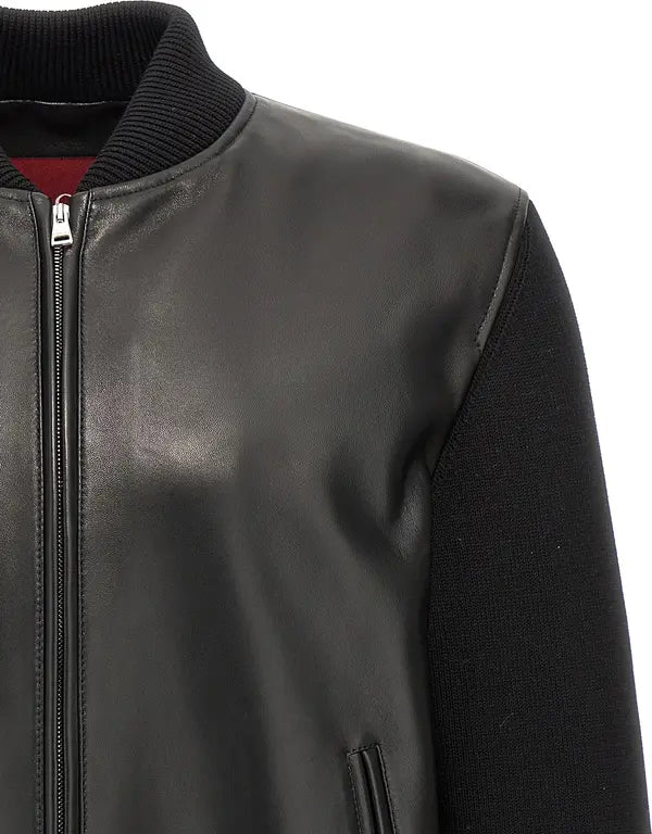 Close-up of a black leather jacket with a ribbed black knit collar and black knit sleeves, featuring a silver zipper and a red inner lining visible at the neckline.