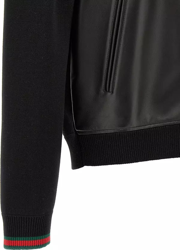Close-up of a black jacket with a ribbed knit sleeve featuring a green and red stripe, a black leather-look panel, and a black ribbed hem on a white background.