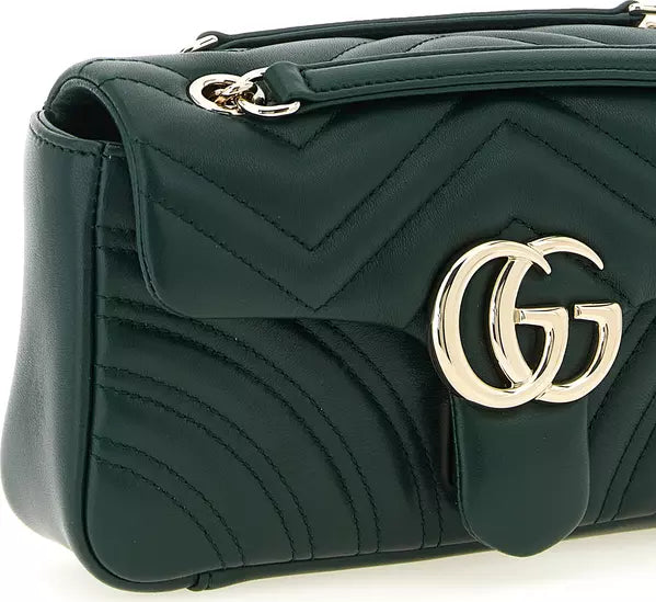 A close-up of a dark green quilted leather handbag featuring a prominent gold-tone interlocking GG logo on the front flap, with matching chain details at the top.