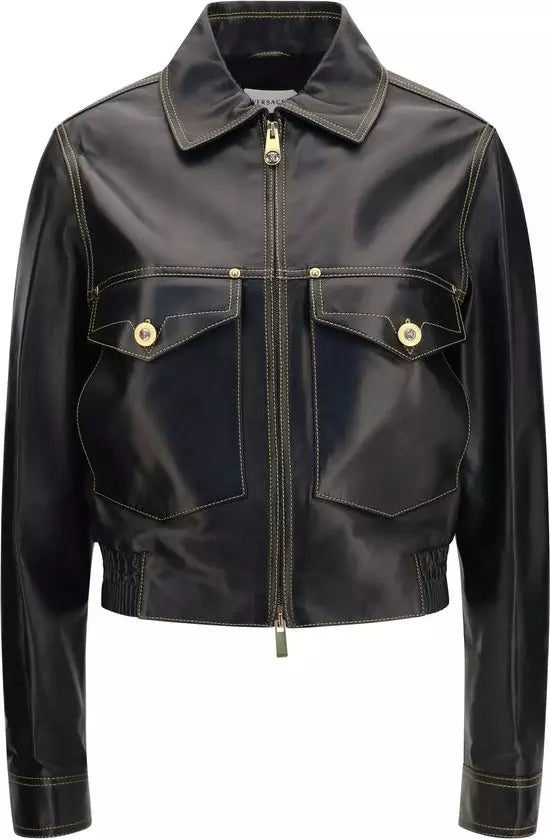 A black leather jacket with gold-toned metal hardware, featuring a zippered front, two buttoned chest pockets, and a pointed collar, shown against a plain white background.