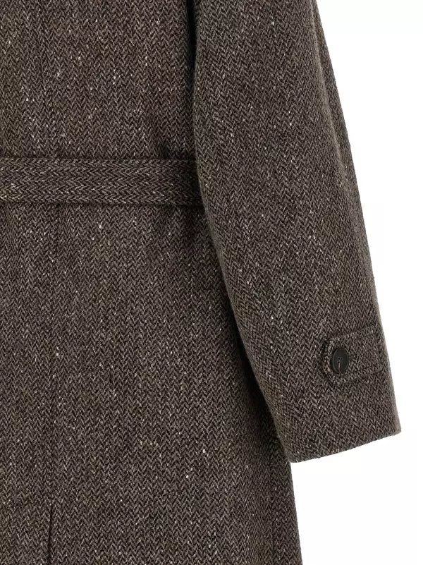 Close-up of a brown herringbone tweed coat with a matching waist belt and a buttoned cuff on a white background.