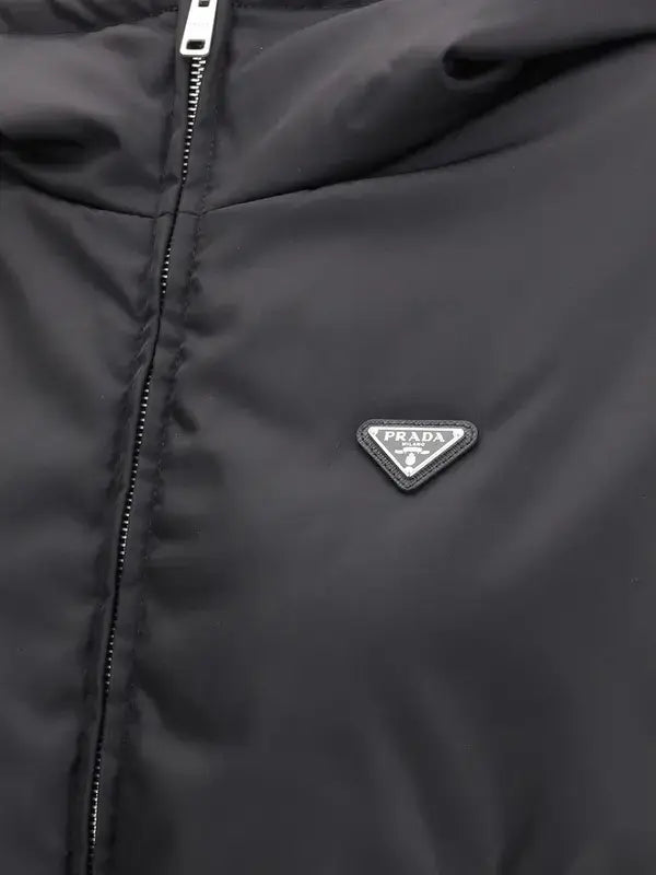 Close-up of a black Prada puffer jacket featuring a silver-tone metal zipper and the iconic triangular Prada logo patch on the chest.