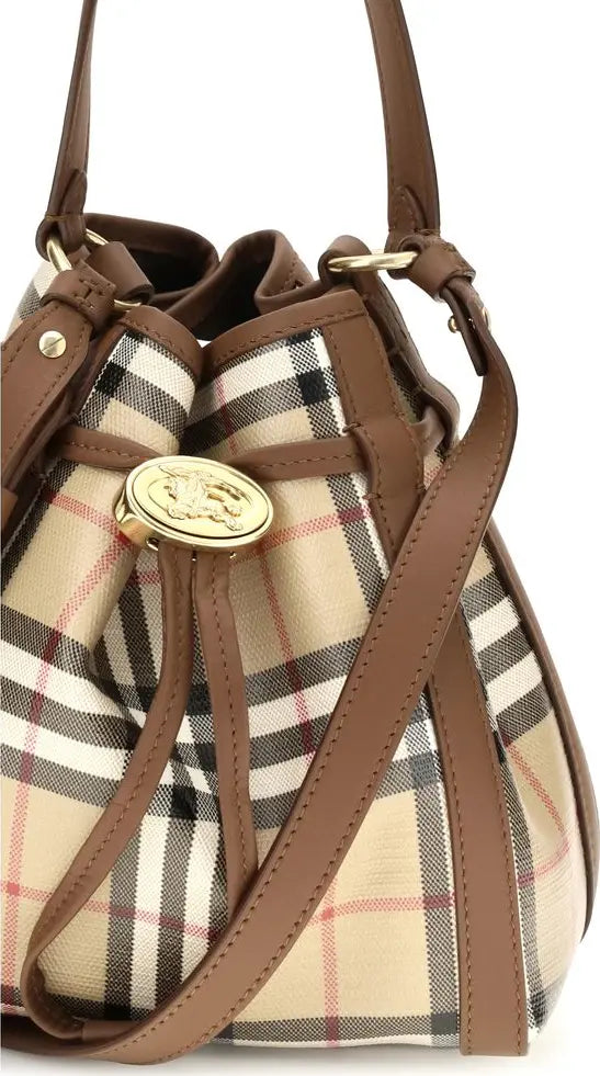 A close-up of a vintage-style plaid bucket bag with brown leather trim and a gold-tone logo clasp, featuring a beige, brown, black, and red check pattern.