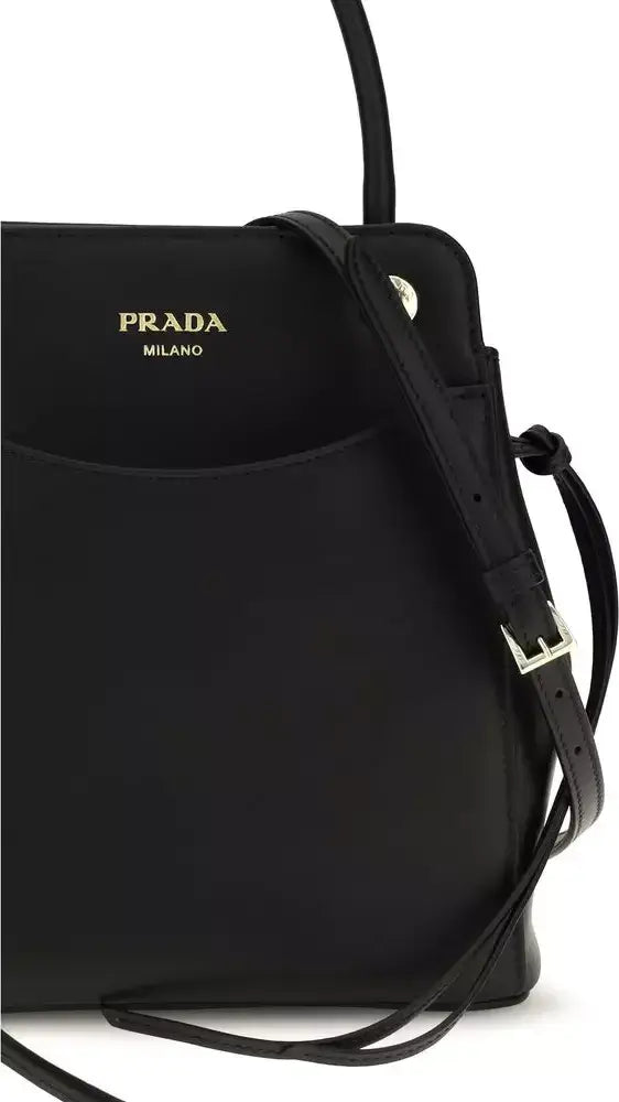 A close-up of a black Prada Milano shoulder bag with gold lettering on the front pocket and a black leather strap with a silver buckle, set against a plain white background.