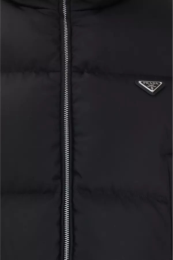 Close-up of a black puffer jacket with a silver zipper and a small silver Prada logo badge on the chest.