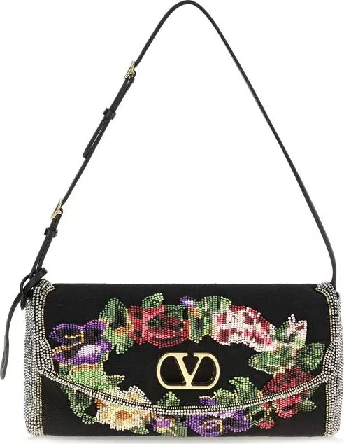 A black leather shoulder bag with a wide flap covered in colorful floral beadwork and rhinestone trim, featuring a gold-tone interlocking V logo on the front.