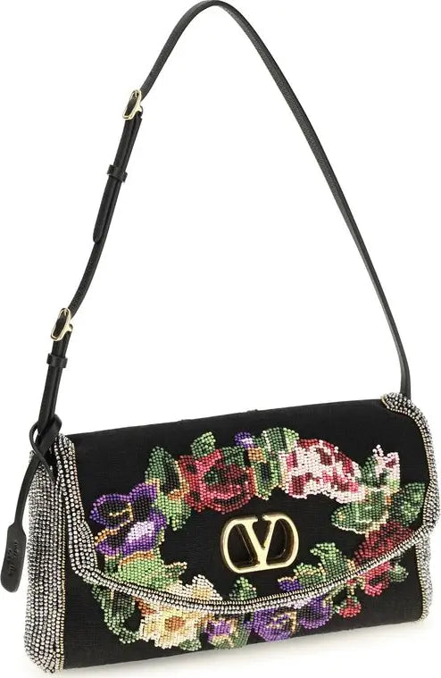 A black velvet shoulder bag with a gold-tone V logo clasp, decorated with a colorful floral embroidered pattern and embellished with rhinestones along the edges and strap.