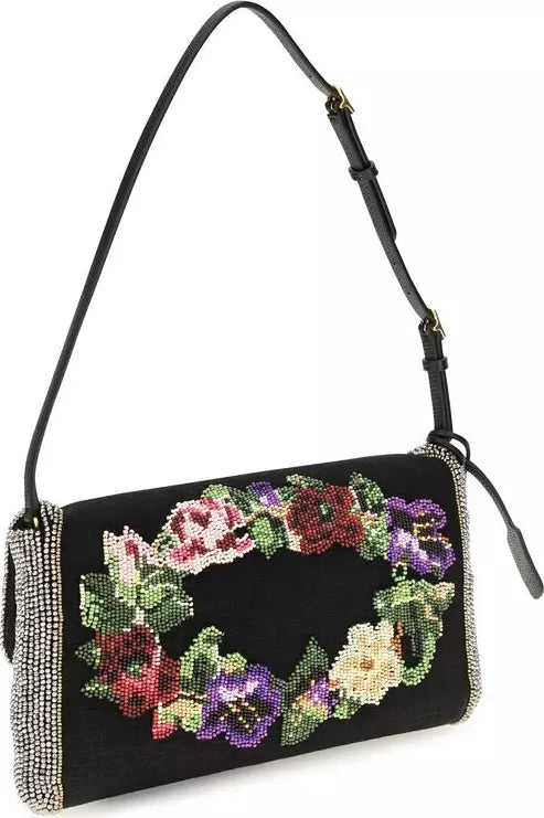A black shoulder bag with a beaded floral wreath design on the front flap, featuring purple, red, green, and cream flowers, a black leather strap, and silver rhinestone trim on a white background.