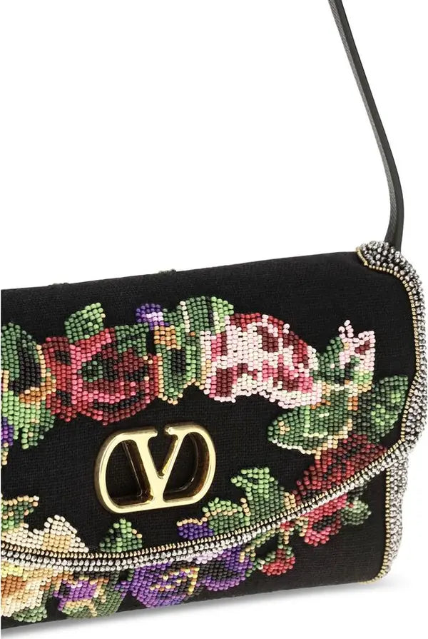 Close-up of a black handbag with a colorful beaded floral pattern and a gold-tone interlocking V logo on the front, against a white background.