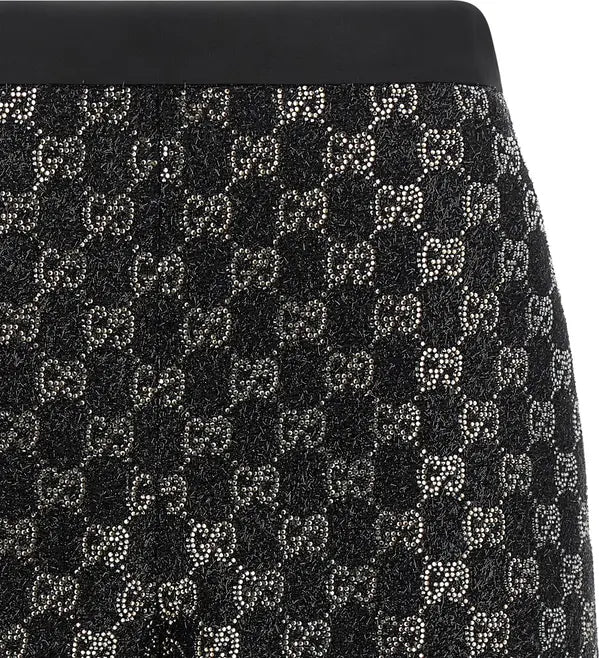 Close-up of a black skirt featuring a repeating Gucci GG monogram pattern embellished with sparkling rhinestones, finished with a solid black waistband.