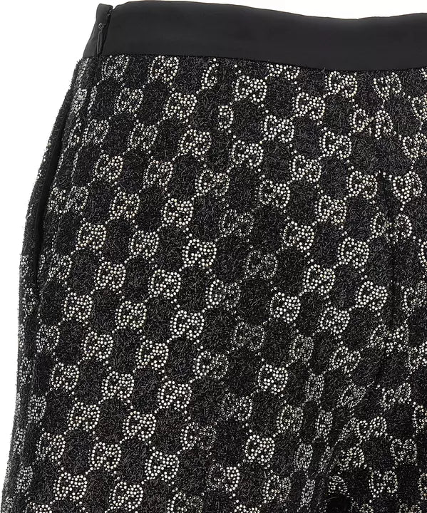 Close-up of a black skirt featuring a repeating Gucci GG monogram pattern made of small white and silver rhinestones, with a solid black waistband.