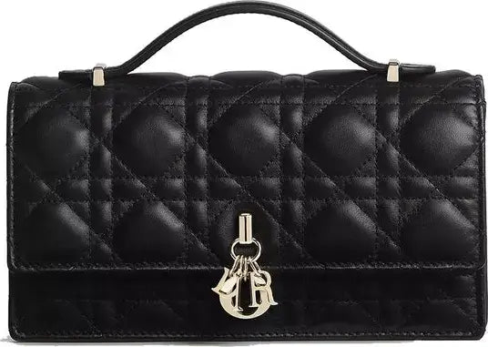 A black quilted leather handbag with a top handle and a gold-tone Christian Dior CD charm on the front flap, set against a plain white background.