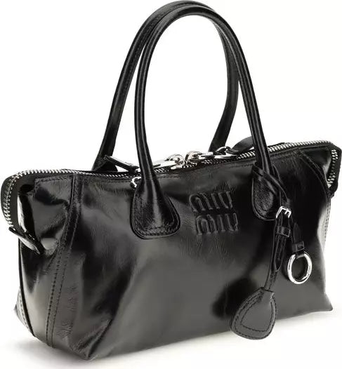 A black patent leather Miu Miu handbag with double top handles, a top zipper, and silver-tone hardware, shown on a white background.