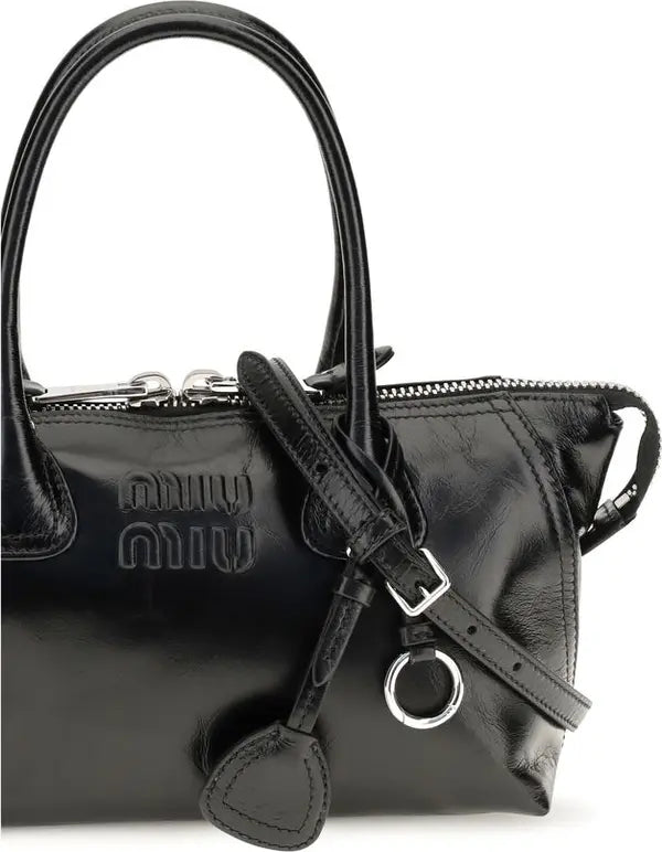 Black Miu Miu leather handbag with a top handle, zippered closure, and embossed logo on a white background.