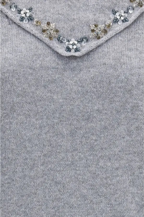 Close-up of a light gray knit sweater featuring a V-neckline embellished with small floral bead and crystal patterns.